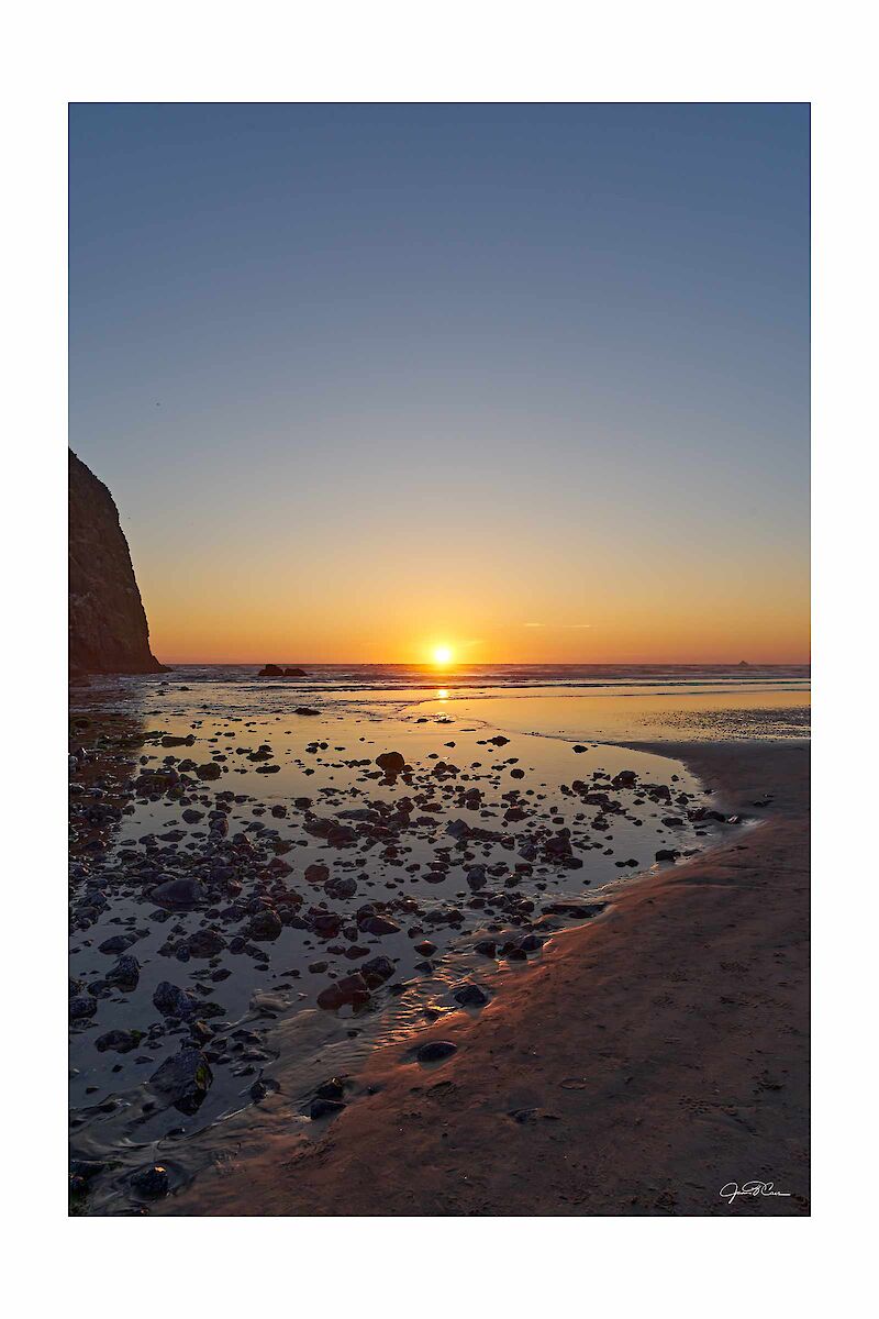 The sun begins to dip below the ocean horizon behind Haystack Rock in Cannon Beach, OR